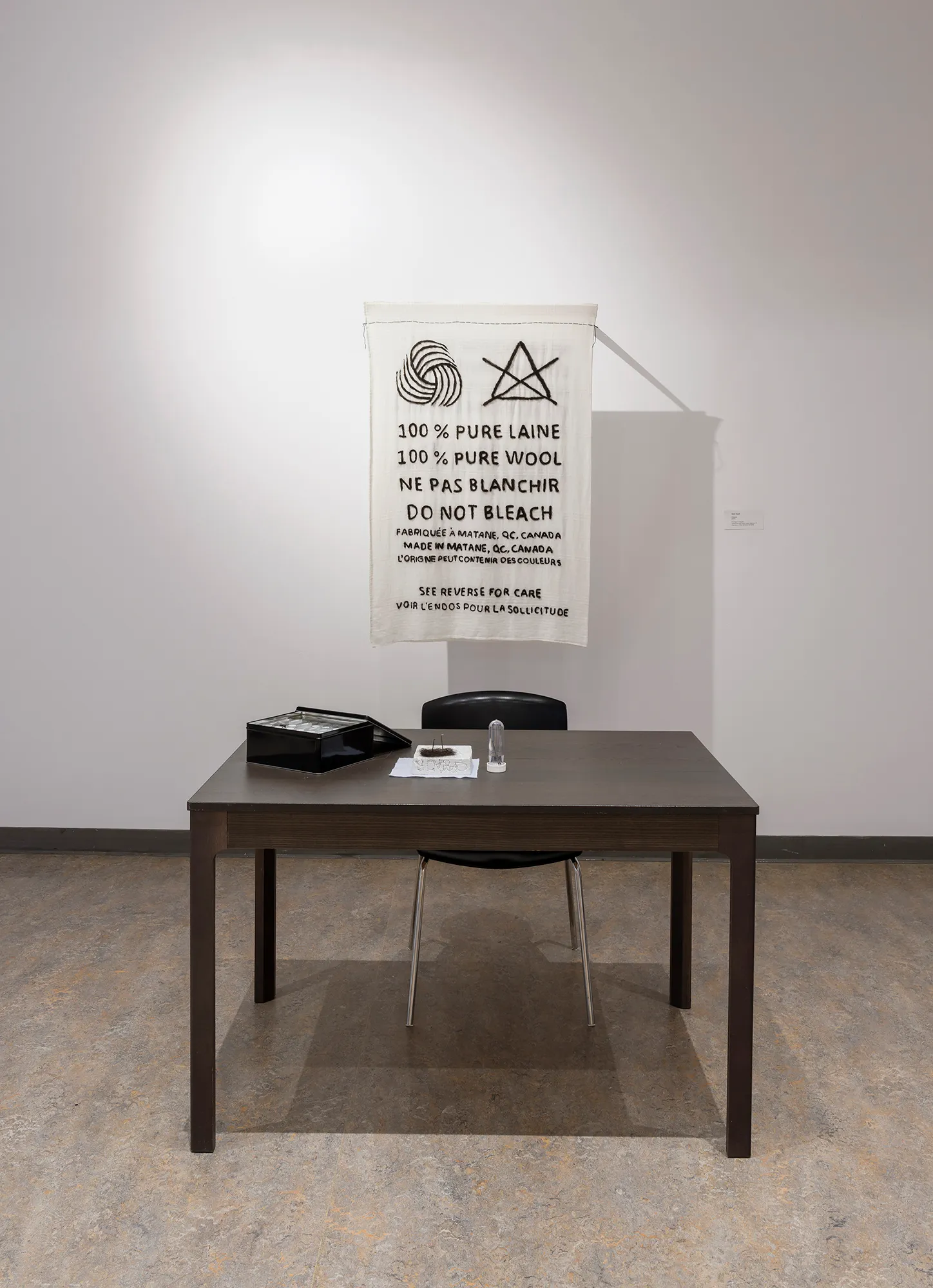 Nadia Gagné, Étiquette, 2023, Performance de longue durée de feutrage à l’aiguille sur nappe de coton blanc tissé, cheveux, fil d’acrylique, latte de bois et aimants
