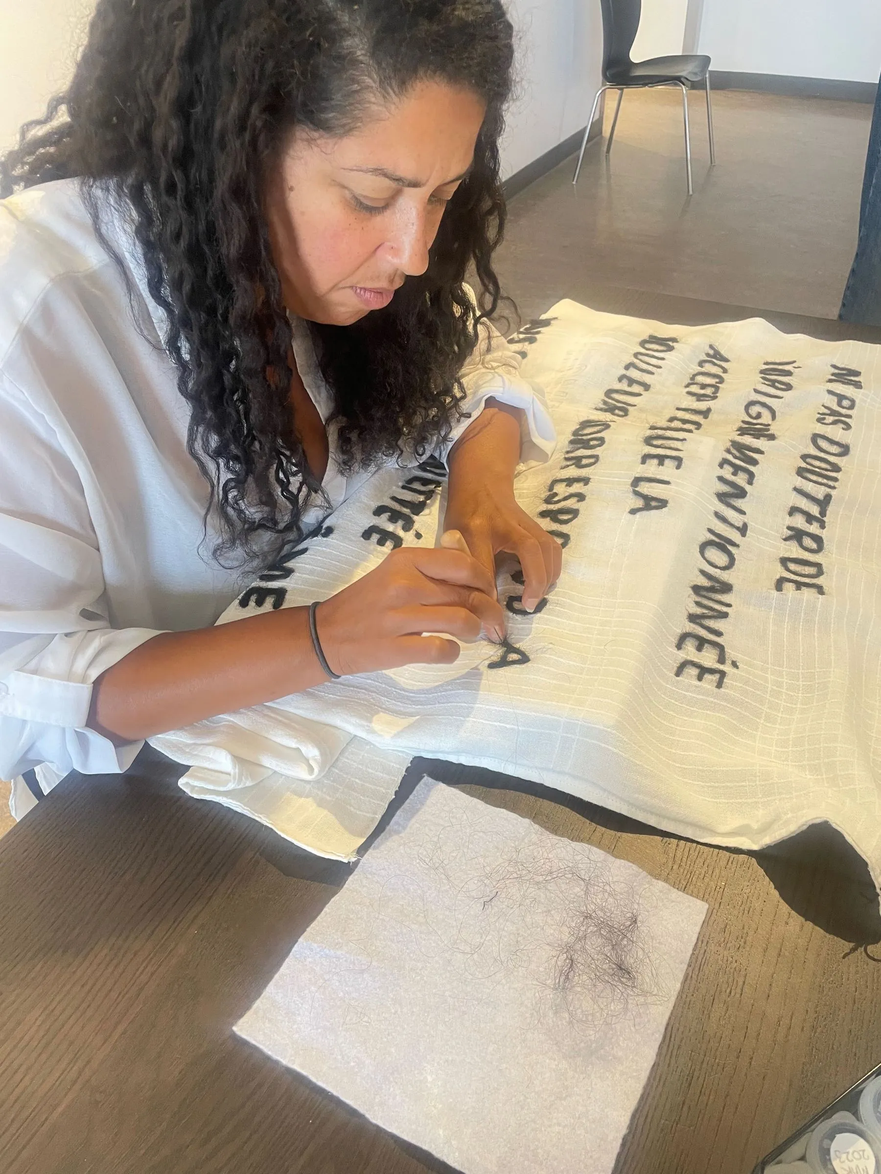 Nadia Gagné, Étiquette, 2023. Performance de longue durée de feutrage à l’aiguille sur nappe de coton blanc tissé, cheveux, fil d’acrylique, latte de bois et aimants
